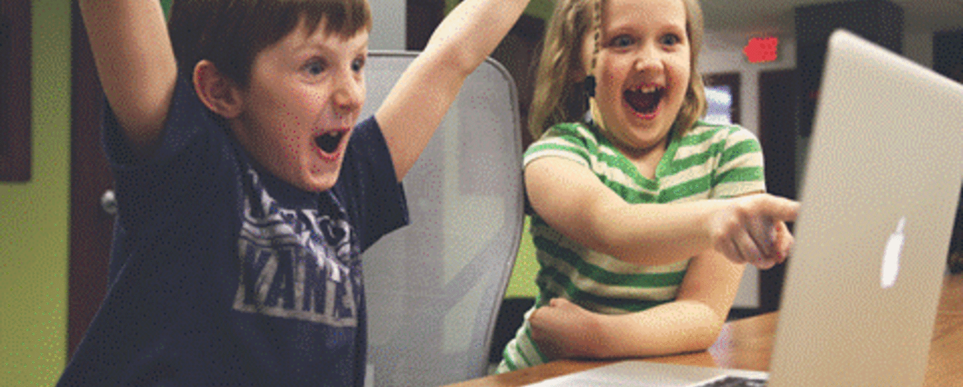 Image: two kids, boy and girl, ecstatic over something visible to them on computer screen