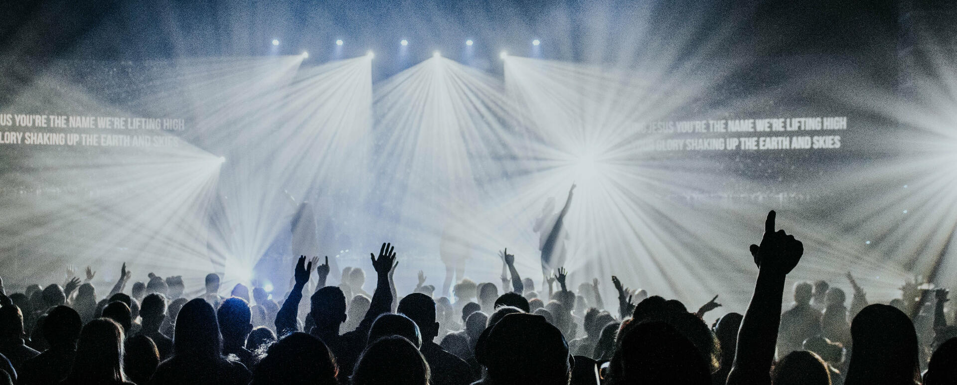 A crowd at the festival. Shapes of the attendees, many with their hands in the air, are standing out against the stage lights in the background