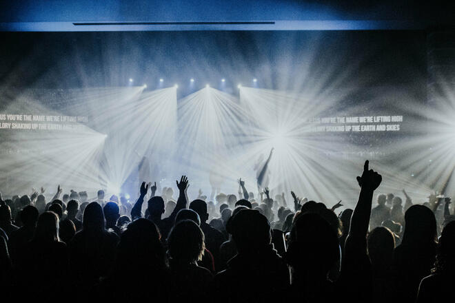 A crowd at the festival. Shapes of the attendees, many with their hands in the air, are standing out against the stage lights in the background
