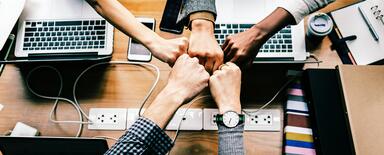 Five stretched hands over the desk doing fist bump in a gesture symbolysing good team and job done