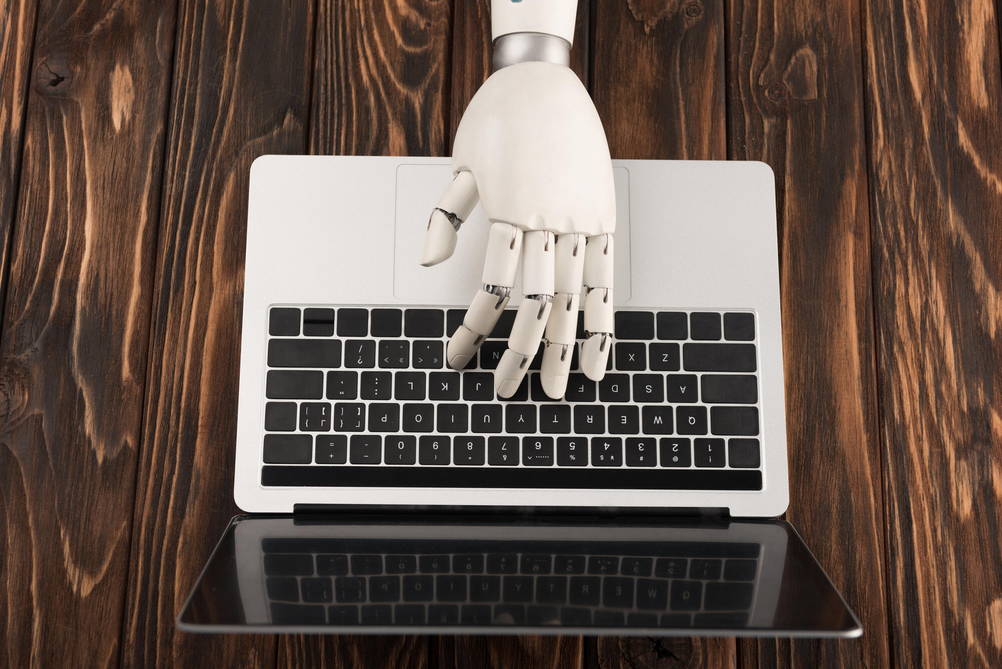 cropped shot of robot working with laptop on wooden surface
